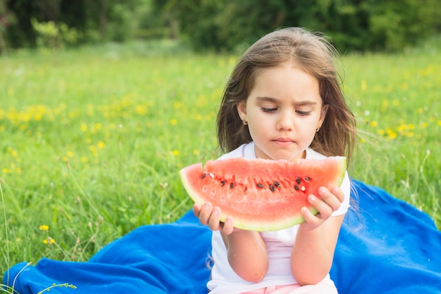 Nahaufnahme eines Mädchens, das Wassermelonenscheibe im Park betrachtet
