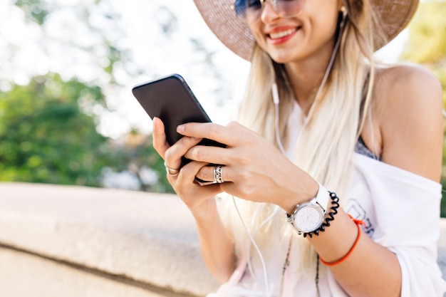 Nahaufnahme eines Mädchens mit einem Telefon und Kopfhörern, die Musik und Lächeln hören. Hübsches Mädchen hält ihr Telefon und sendet Nachricht mit großen Emotionen.