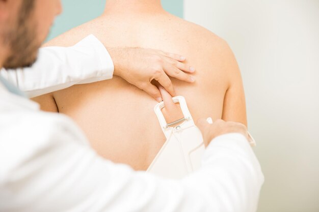 Nahaufnahme eines männlichen Ernährungsberaters, der Körperfett und Falten im Rücken eines Patienten in einer Gesundheitsklinik misst