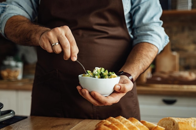 Nahaufnahme eines Mannes, der eine Schüssel mit Avocado hält, während er gesundes Essen in der Küche zubereitet