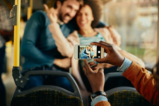 Nahaufnahme eines Mannes, der glückliches Paar mit Handy in einem Bus fotografiert