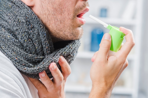 Kostenloses Foto nahaufnahme eines mannes, der grauen schal um seinen hals unter verwendung eines sprays trägt, um halsschmerzen zu behandeln