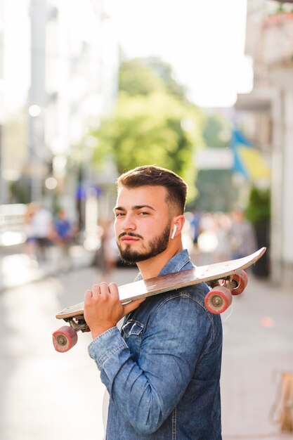 Nahaufnahme eines Mannes mit dem Skateboard, das Kamera betrachtet