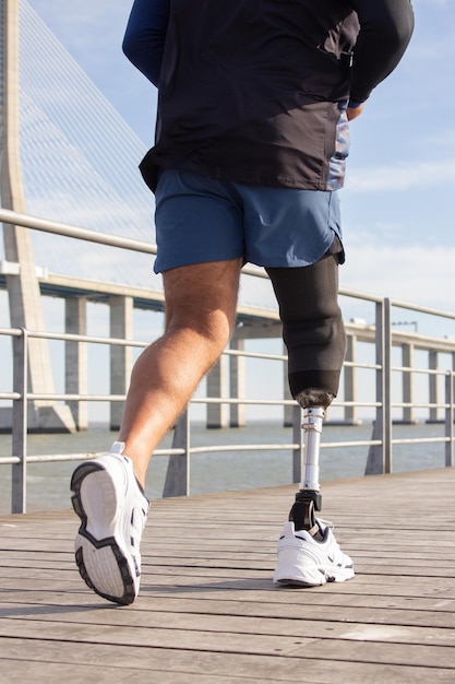 Kostenloses Foto nahaufnahme eines mannes mit mechanischem beinlauf. sportler in blauen shorts und weißen turnschuhen beim joggen fotografiert. sport, hobby, behinderungskonzept