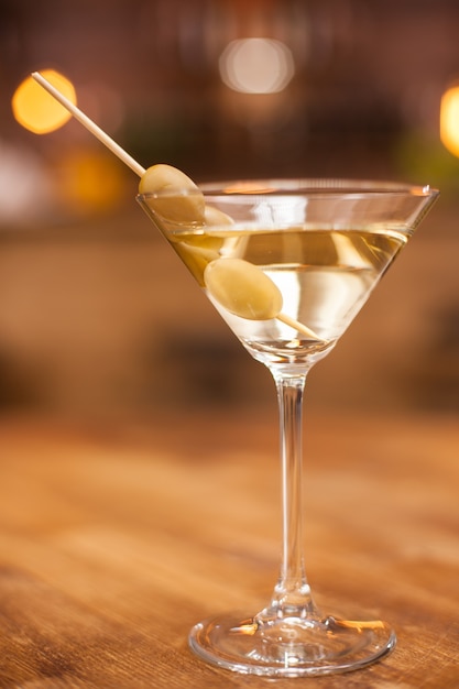 Nahaufnahme eines Martini-Glases mit Oliven auf einem Holztisch in einem Restaurant. Frisches Getränk. Leckeres Getränk. Alkoholisches Getränk.