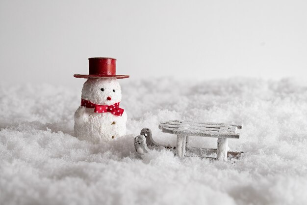 Nahaufnahme eines niedlichen Schneemannspielzeugs und eines Schlittens im Schnee,