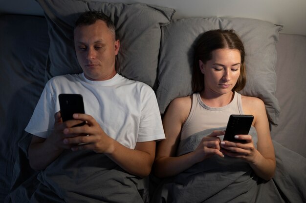 Nahaufnahme eines Paares auf Telefonen im Schlafzimmer