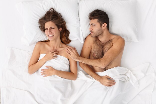 Nahaufnahme eines Paares, das unter einer weißen Decke im Bett liegt