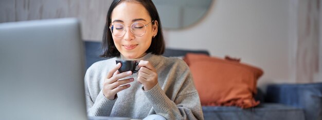 Nahaufnahme eines Porträts einer schönen asiatischen Frau, die ihren Kaffee trinkt und in einer Tasse riecht