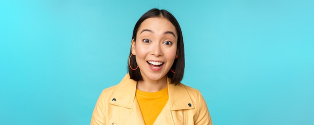 Nahaufnahme eines Porträts eines natürlichen asiatischen Mädchens, das lacht, lächelt und glücklich über blauem Backgr steht