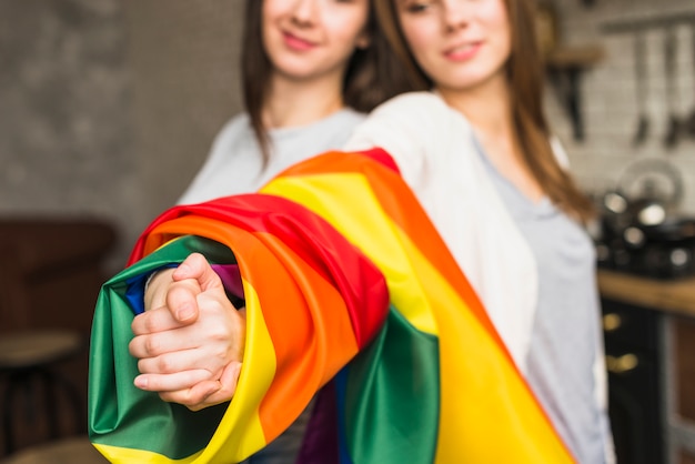 Kostenloses Foto nahaufnahme eines reizenden lesbischen jungen paares, das hände mit eingewickelter lgbt-stolzflagge sich hält