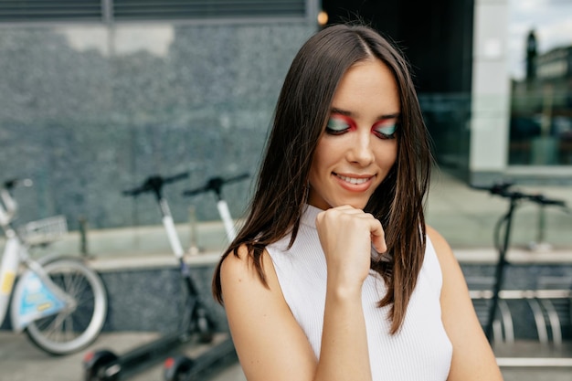 Kostenloses Foto nahaufnahme eines romantischen hübschen mädchens mit hellem urlaubs-make-up, das mit geschlossenen augen und schüchternem lächeln vor stadthintergrund in die kamera posiert