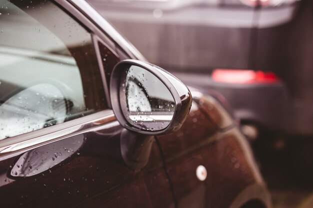 Nahaufnahme eines Rückspiegels eines braunen Autos bedeckt in Regentropfen mit einem verschwommenen Hintergrund