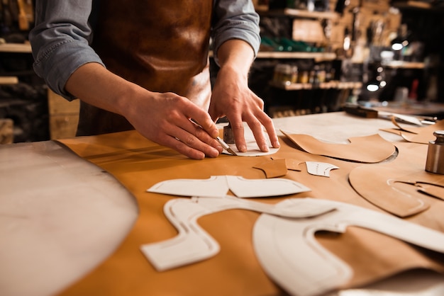 Nahaufnahme eines Schuhmachers, der Leder misst und schneidet