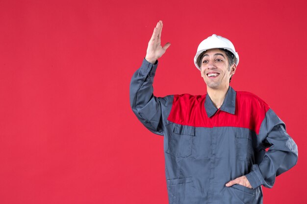 Nahaufnahme eines selbstbewussten jungen Architekten in Uniform mit Schutzhelm und nach oben auf isolierte rote Wand zeigend