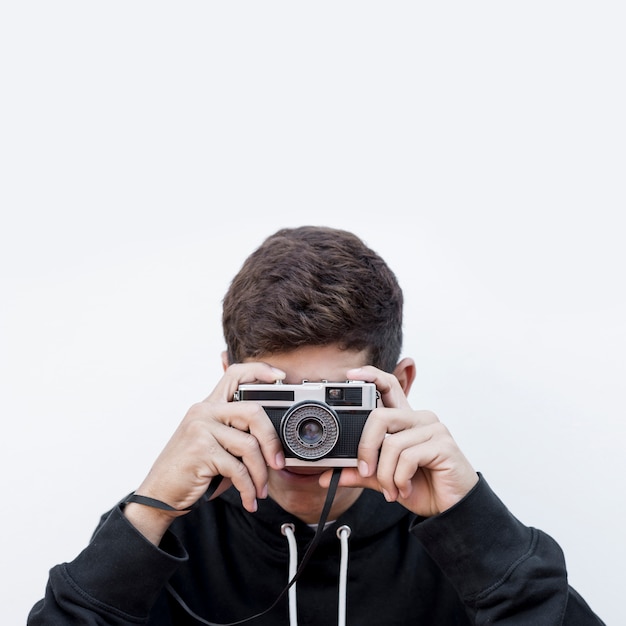 Nahaufnahme eines teenagers, der fotografie nimmt, klicken auf retro- weinlesefotokamera gegen weißen hintergrund