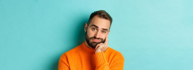 Kostenloses Foto nahaufnahme eines unamüsierten traurigen mannes, der schmollend in die kamera blickt und das gesicht an der hand lehnt, das über licht b steht