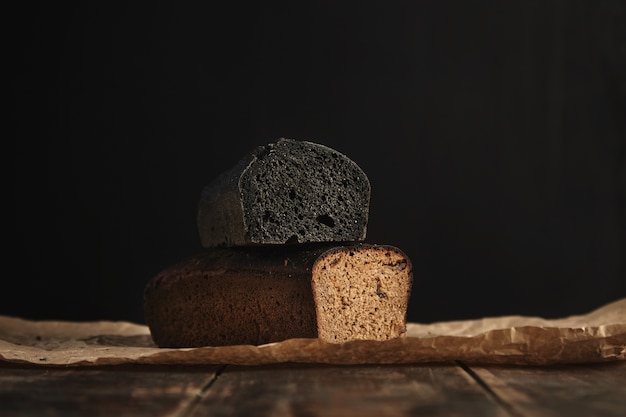 Nahaufnahme Fokus auf zwei frisch gebackene Diät gesunde Brote. Holzkohle und Roggen mit Feigen, isoliert auf Schwarz, präsentiert auf rustikalem Holztisch