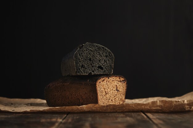 Nahaufnahme Fokus auf zwei frisch gebackene Diät gesunde Brote. Holzkohle und Roggen mit Feigen, isoliert auf Schwarz, präsentiert auf rustikalem Holztisch