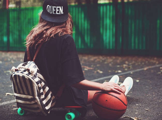 Nahaufnahme Foto Basketballball mit Mädchen sitzen auf Kunststoff orange Penny Shortboard auf Asphalt