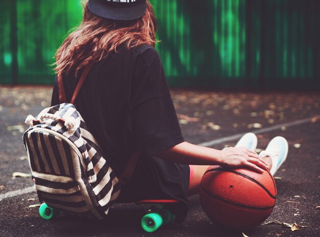 Nahaufnahme Foto Basketballball mit Mädchen sitzen auf Kunststoff orange Penny Shortboard auf Asphalt