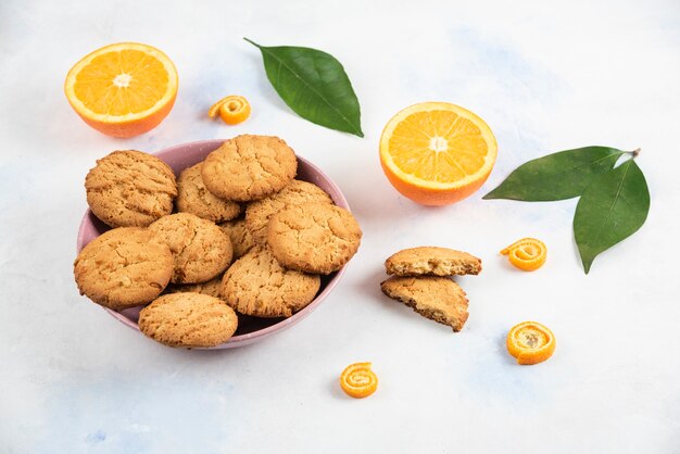 Nahaufnahme Foto frische hausgemachte Kekse in Schüssel und Bio-Orangen im Boden mit Blättern.