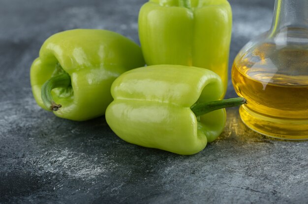 Nahaufnahme Foto von frischen Bio-Paprikaschoten mit einer Flasche Öl auf grauem Hintergrund.