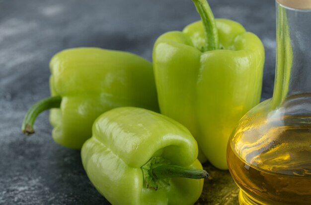 Nahaufnahme Foto von frischen Bio-Paprikaschoten mit einer Flasche Öl auf grauem Hintergrund.