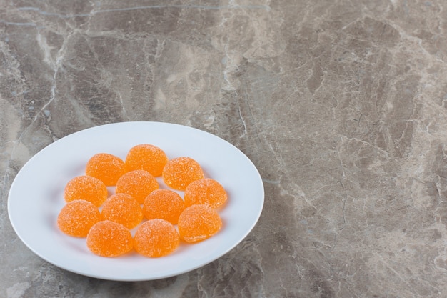 Nahaufnahme Foto von orange Bonbons auf weißem Teller auf grauem Hintergrund.