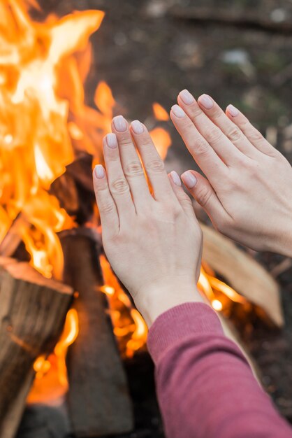 Nahaufnahme Frau, die am Lagerfeuer wärmt