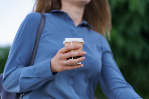 Nahaufnahme Frau Hand in Bewegung mit Kaffee zum Mitnehmen auf Stadtstraße. Porträt blondes Mädchen, das Pappbecher mit heißem Getränk im Freien hält.