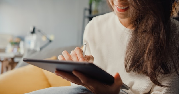 Nahaufnahme freiberufliche asiatische Dame Freizeitkleidung mit Tablet online lernen im Wohnzimmer zu Hause. Arbeiten Sie von zu Hause aus, arbeiten Sie aus der Ferne.