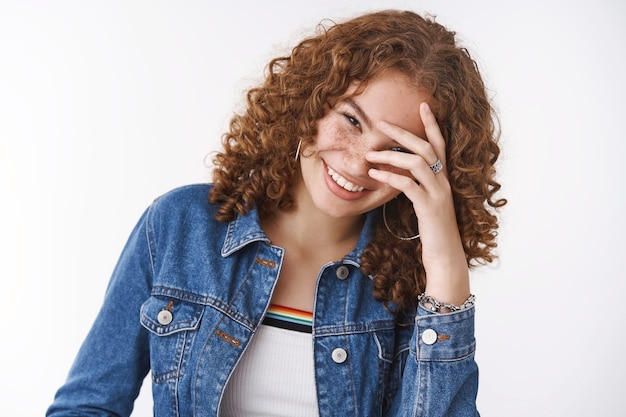 Nahaufnahme freudig positiv lächelnd attraktive junge rothaarige Frau mit Sommersprossen Pickel kippender Kopf lachen sorglos errötend verstecken Gesicht grinsen lustigen Geschichtenwitz hören, stehend weißer Hintergrund