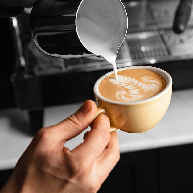 Nahaufnahme Hand, die Milch in Kaffeetasse gießt