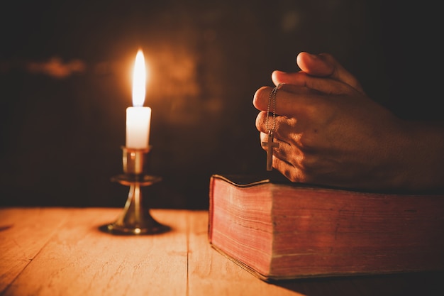 Nahaufnahme herauf die Hand des Mannes betet in der Kirche mit brennender Kerze