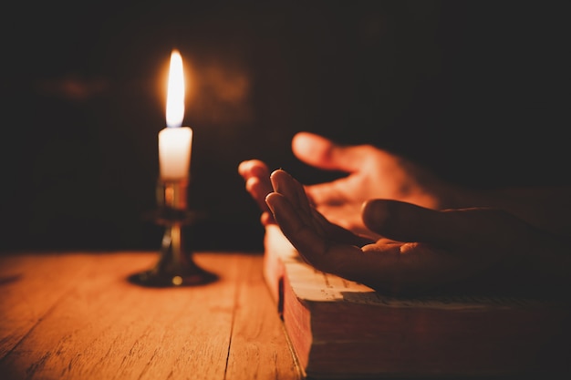 Nahaufnahme herauf die Hand des Mannes betet in der Kirche mit brennender Kerze