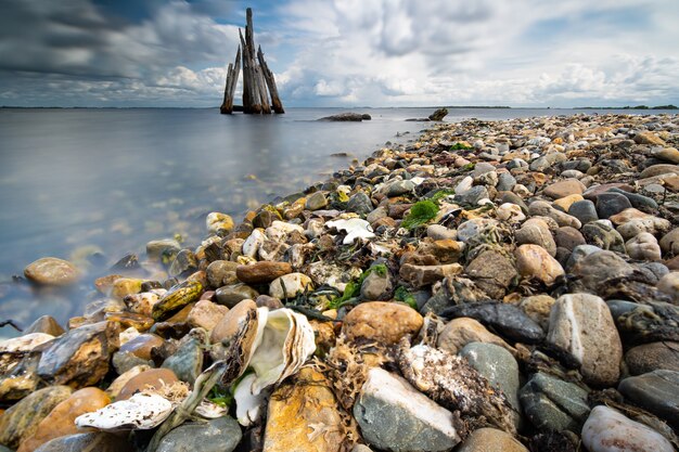 Nahaufnahme hoher Winkelschuss von Steinen an einer Küste mit einem ruhigen Meer auf der Seite unter einem bewölkten Himmel