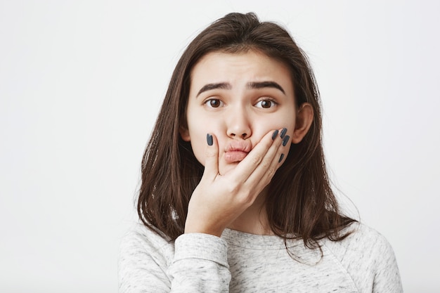 Nahaufnahme junge schöne kaukasische Frau, die ihre Lippen mit der Hand drückt und Augenbrauen anhebt.