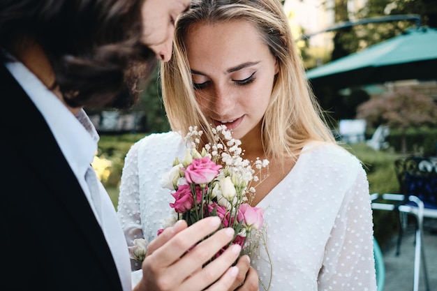 Nahaufnahme junger romantischer Bräutigam und wunderschöne Braut, die sinnlich einen Blumenstrauß im Freien halten