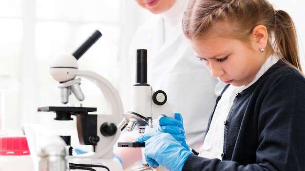 Nahaufnahme Mädchen mit Handschuhen und Mikroskop