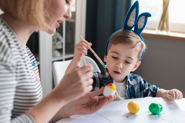 Nahaufnahme Mutter zeigt kleinen Jungen, wie man Eier malt
