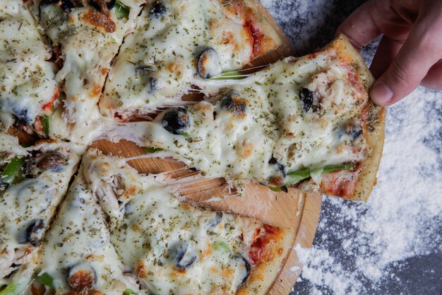 Nahaufnahme Pizza auf einem Holzständer, Hand nehmen ein Stück Pizza horizontal