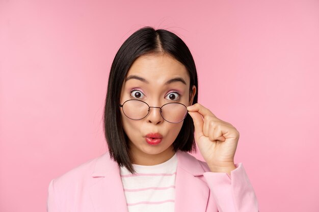 Nahaufnahme Porträt der koreanischen Bürodame nimmt Brille ab und schaut beeindruckt in die Kamera überraschter Gesichtsausdruck rosa Hintergrund