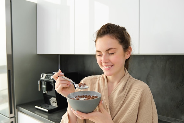 Nahaufnahme Porträt einer lächelnden schönen Frau, die Müsli mit Milch isst und einen Löffel und eine Schüssel hält