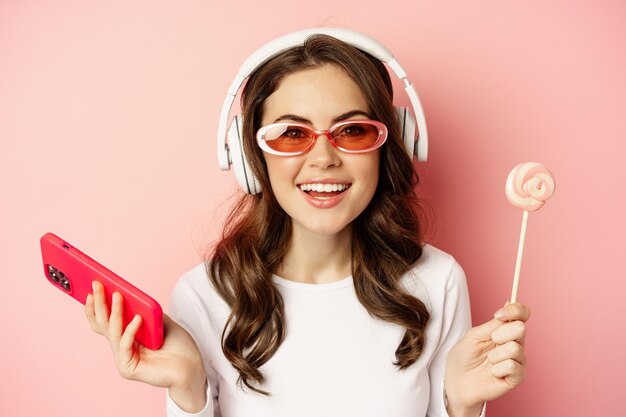 Nahaufnahme Porträt einer schönen Frau mit stilvollem Glamour-Mädchen in Kopfhörern, die Musik mit Smartphone hört ...