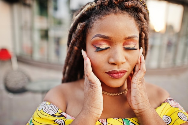 Nahaufnahme Porträt eines afrikanisch-amerikanischen Mädchens kleiner Größe mit Dreadlocks auf farbigem gelbem Kleid Gesicht mit Make-up