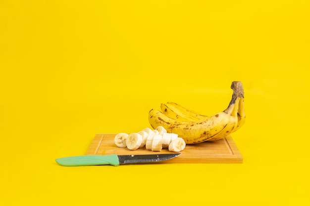 Nahaufnahme reifer Bananen auf einem Schneidebrett mit einem Messer darauf isoliert auf gelbem Hintergrund
