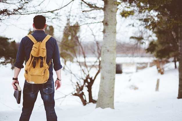 Nahaufnahme schoss von hinten von einem Mann, der einen gelben Rucksack trägt und die Bibel hält