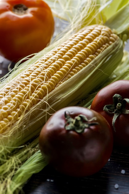 Kostenloses Foto nahaufnahme schuss von frischem mais mit blei auf einem tisch mit drei tomaten aufgestellt