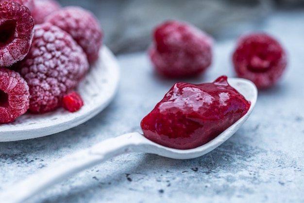 Nahaufnahme Schuss von Himbeermarmelade mit gefrorenen Himbeeren im Hintergrund